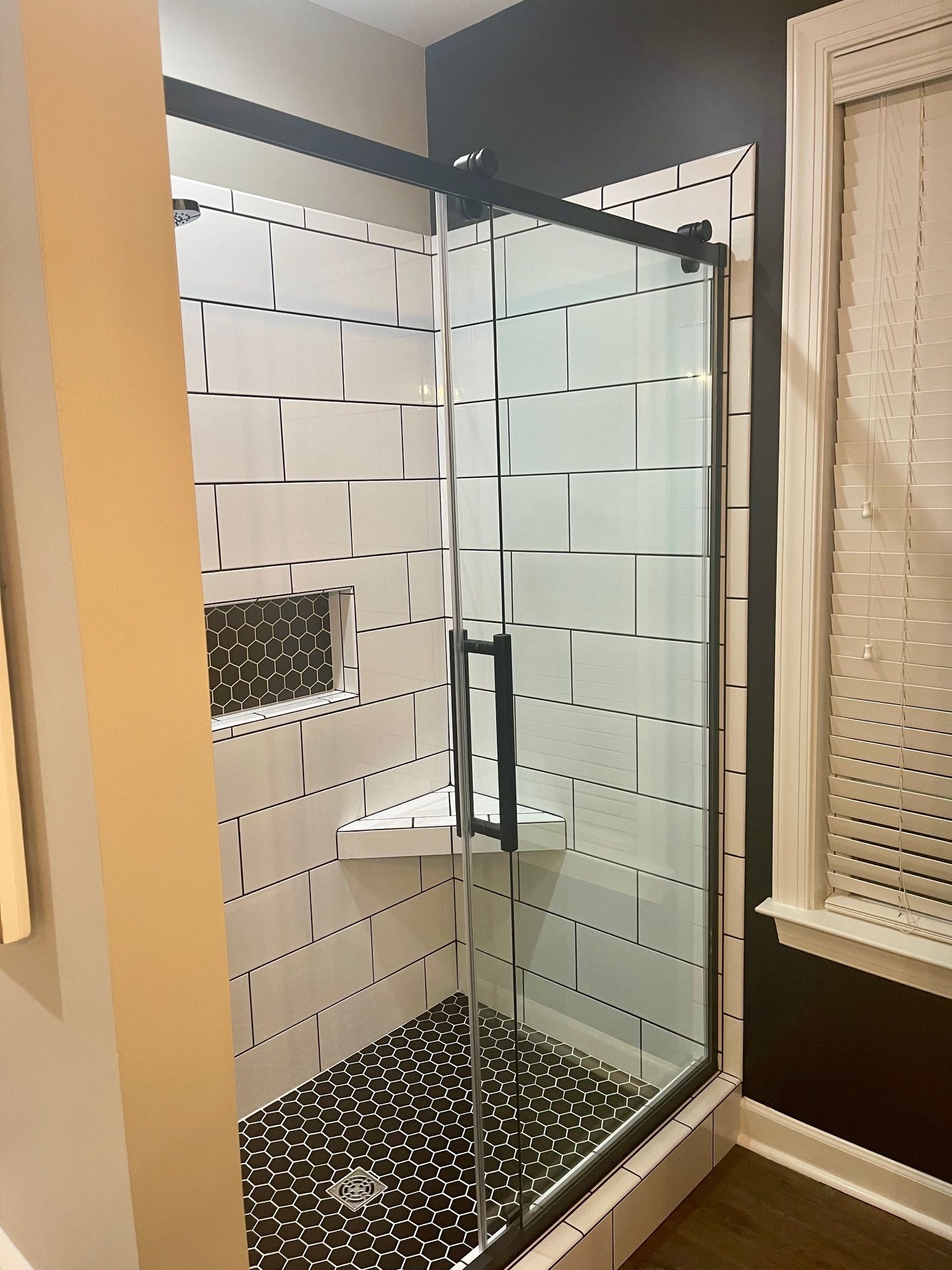 Modern bathroom shower with black framed glass door, white tiled walls, and black pebble floor.