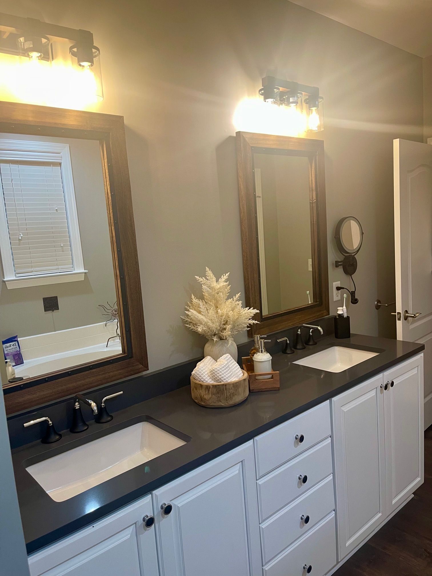 Bathroom with white cabinets, dark countertop, two sinks, mirrors, and decorative items.