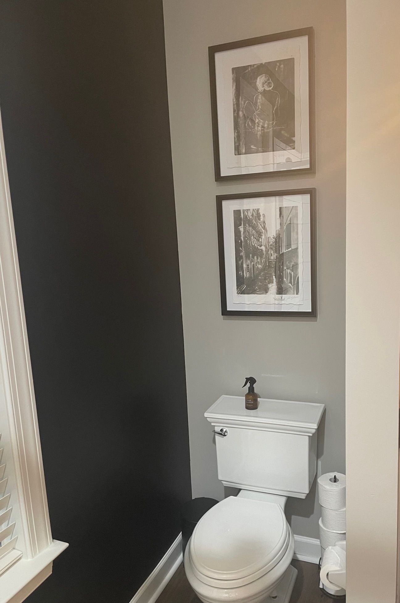 A small bathroom with a black accent wall and gray walls. Two framed art pieces above the toilet.