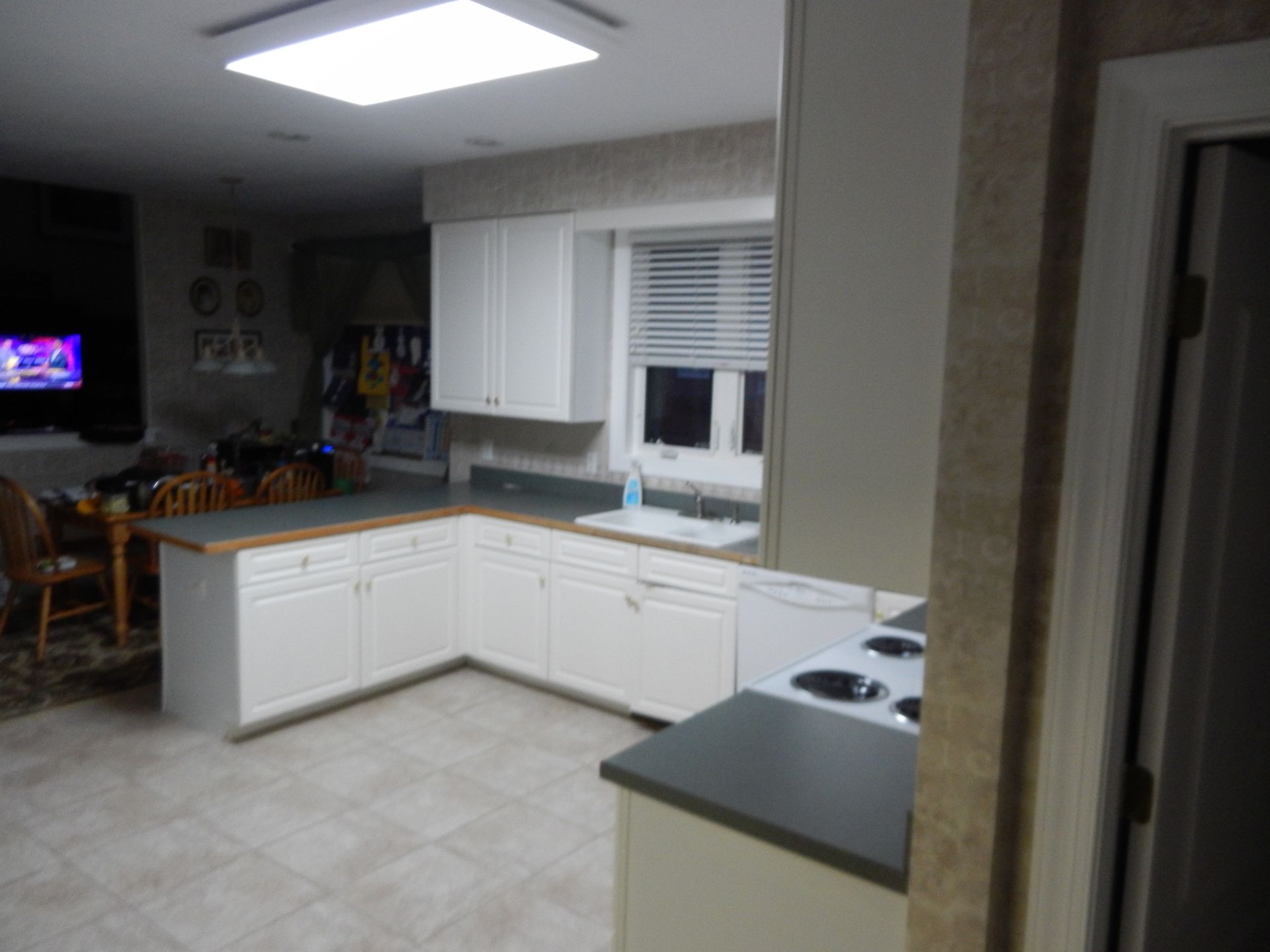 L-shaped kitchen with white cabinets, gray countertops, and a window. Dining area visible in the background.