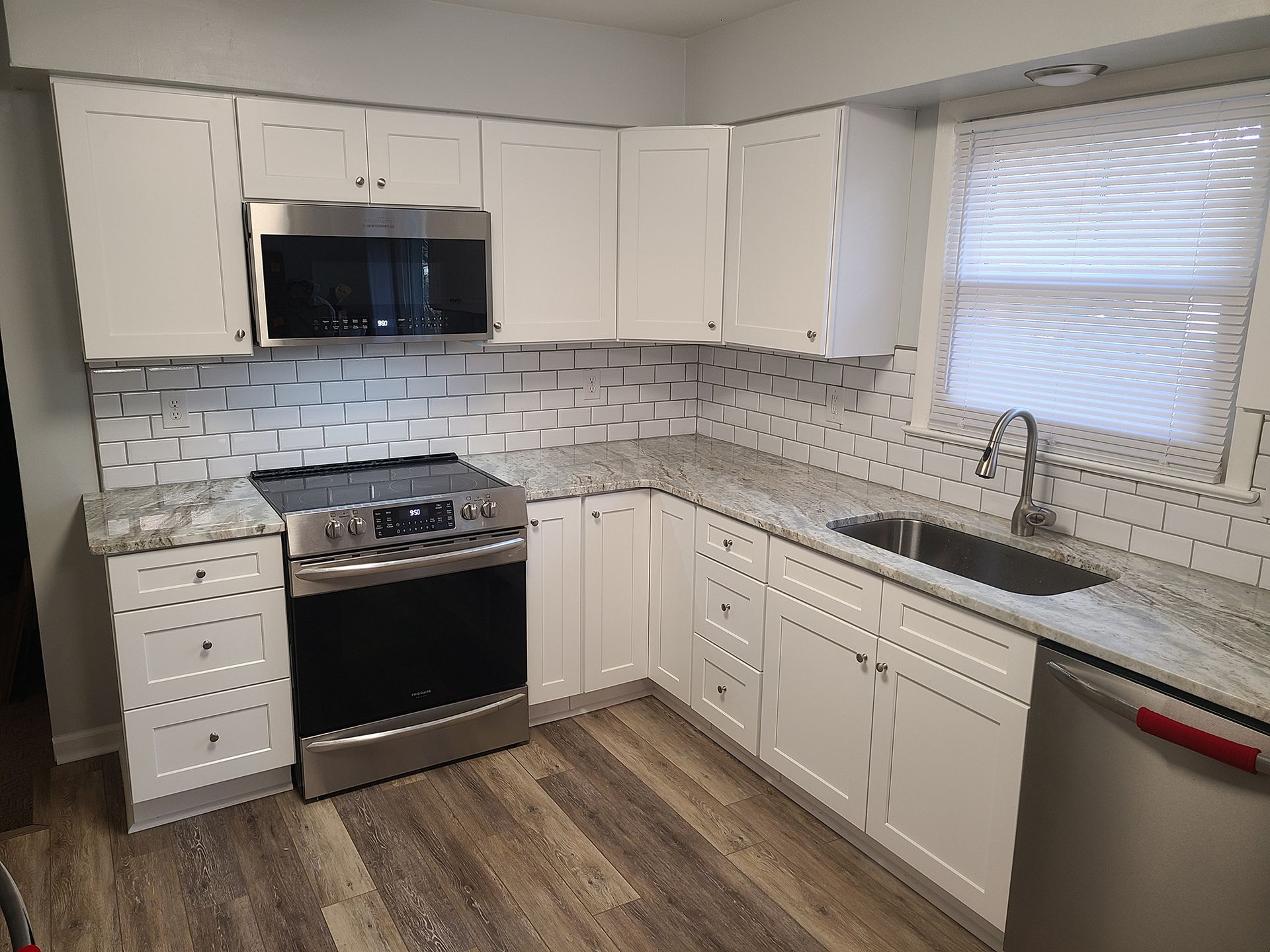 White kitchen with stainless steel appliances, granite countertops, and wood-look flooring.