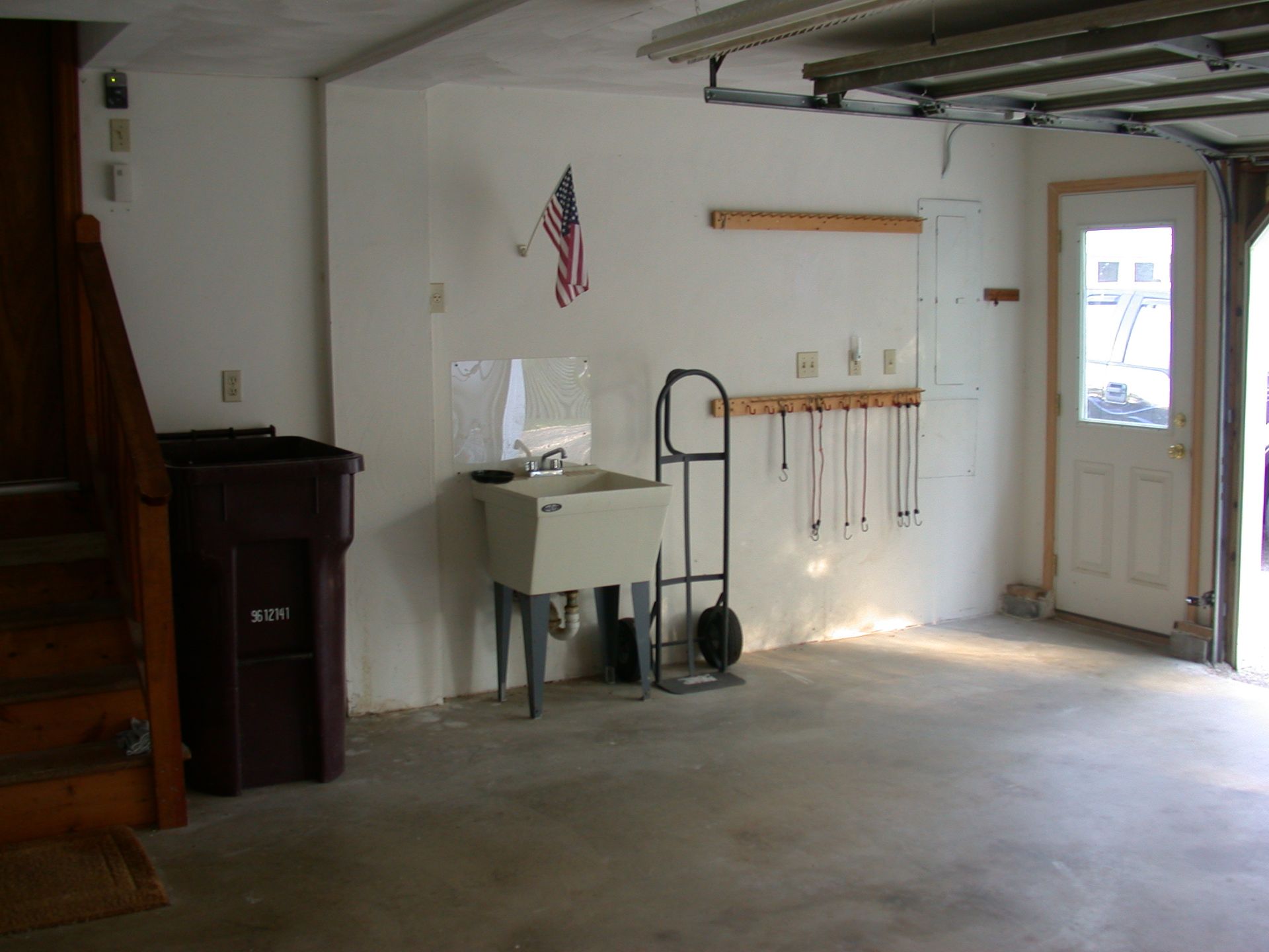 Garage interior with a utility sink, trash can, and garage door. American flag hanging on the wall.