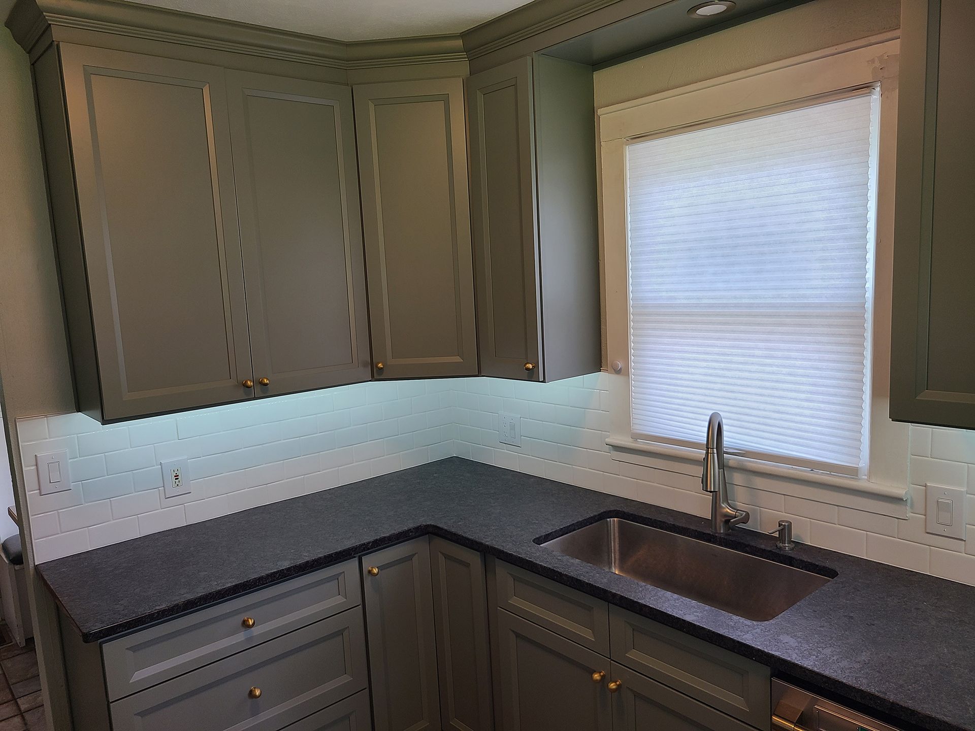 Gray kitchen with cabinets, dark countertops, sink, and window with blinds.