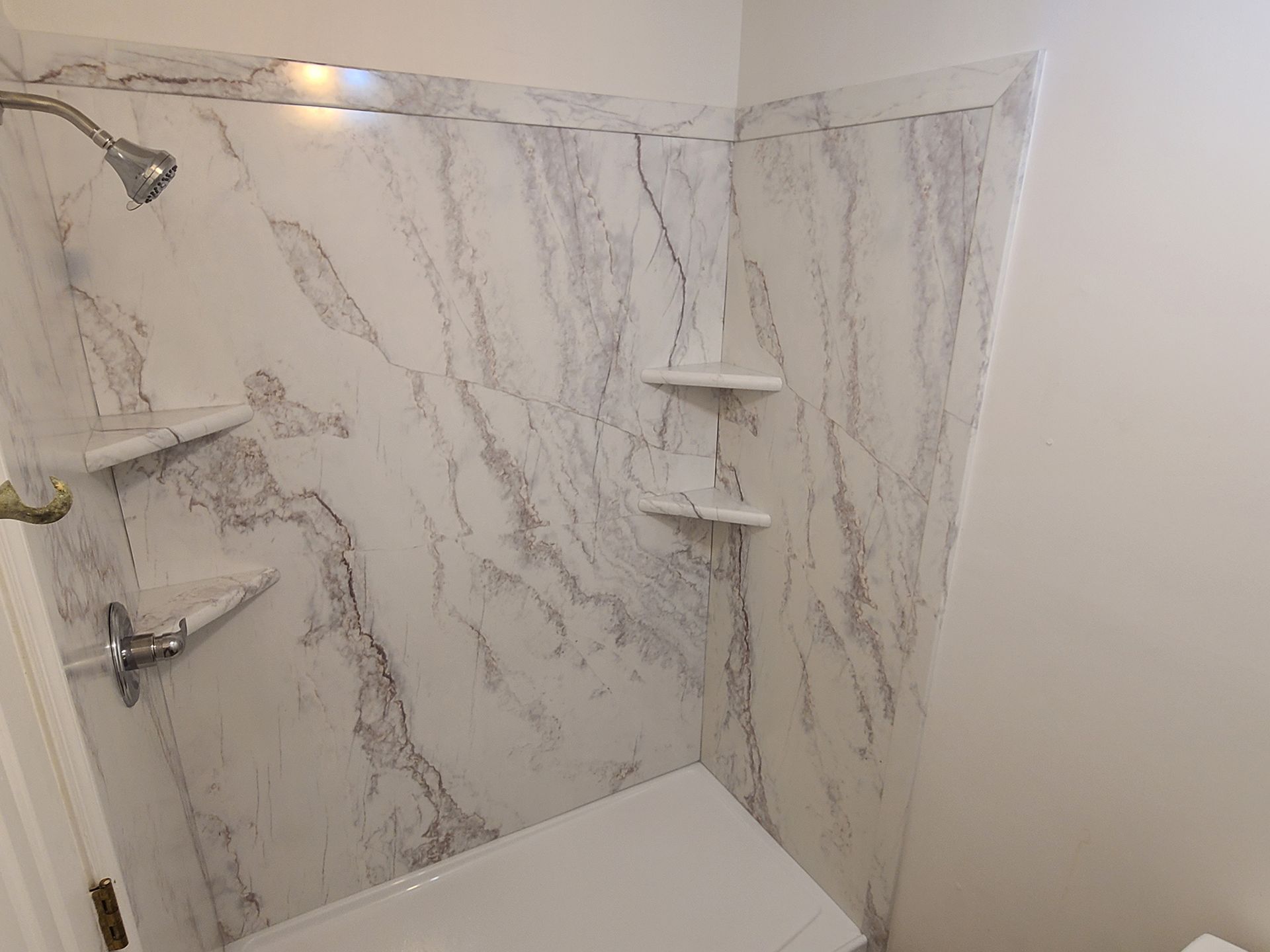 Shower stall with marble-patterned walls, built-in shelves, and a showerhead.