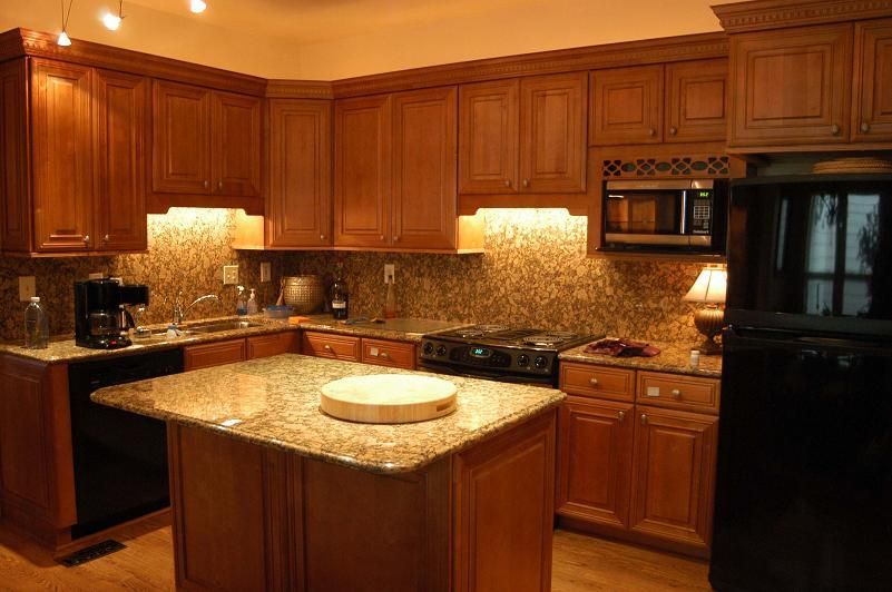 A kitchen with wooden cabinets , granite counter tops , a stove and a refrigerator.