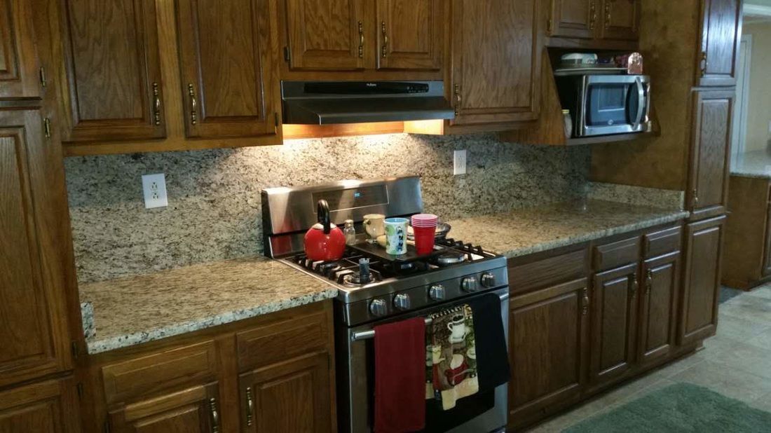 A kitchen with wooden cabinets , granite counter tops , a stove and a microwave.