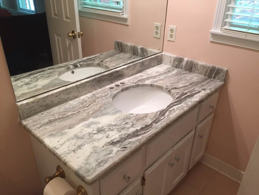 A bathroom with a sink , mirror and marble counter top.