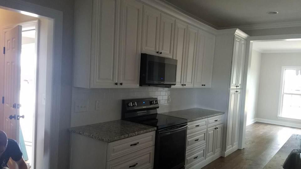 A kitchen with white cabinets , a stove , and a microwave.