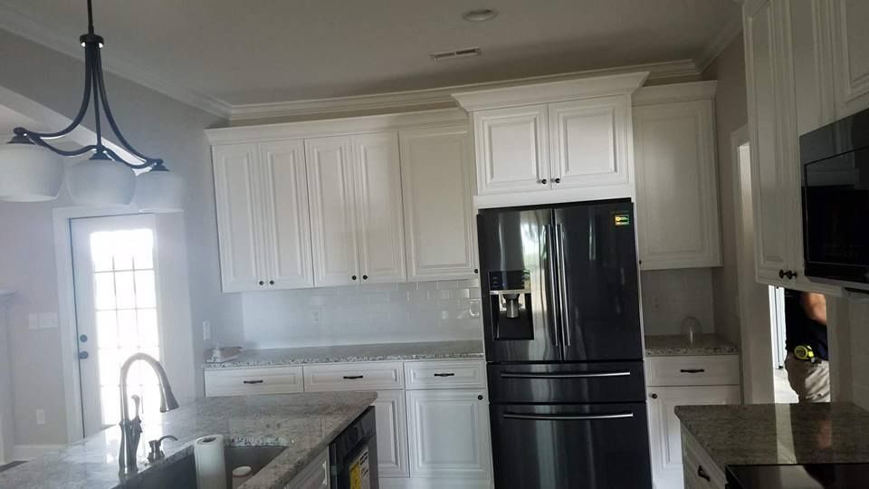 A kitchen with white cabinets and a black refrigerator.