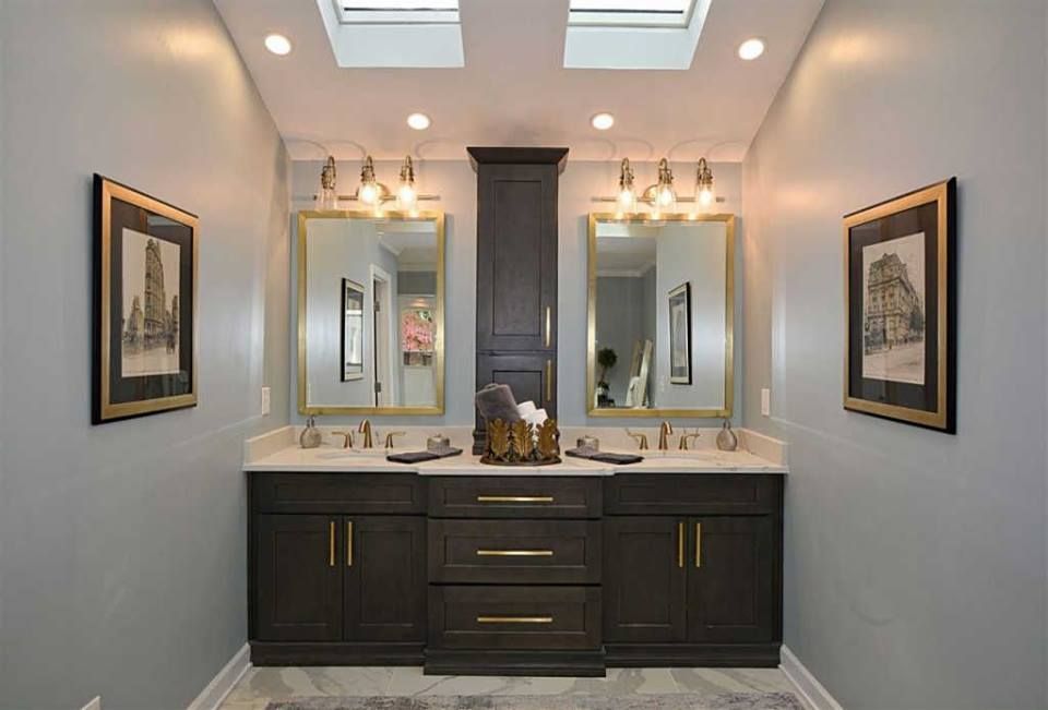 A bathroom with two sinks , two mirrors and a skylight.