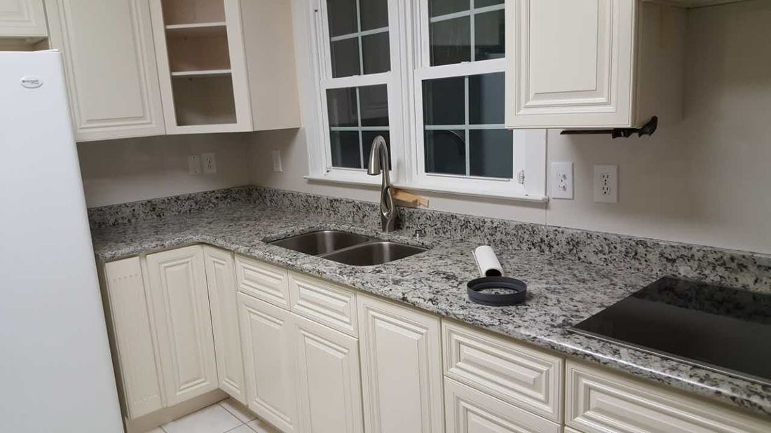 A kitchen with granite counter tops , white cabinets , a sink and a stove.