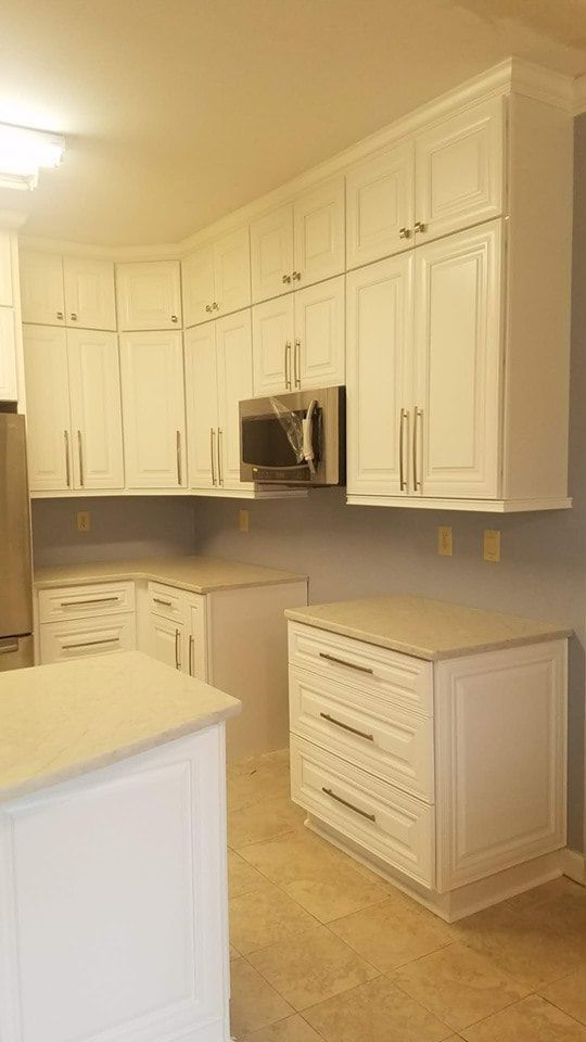 A kitchen with white cabinets , a microwave , and a refrigerator.