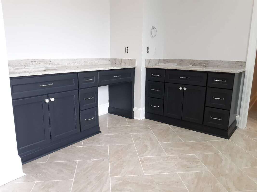 A bathroom with two sinks , a desk , and black cabinets.