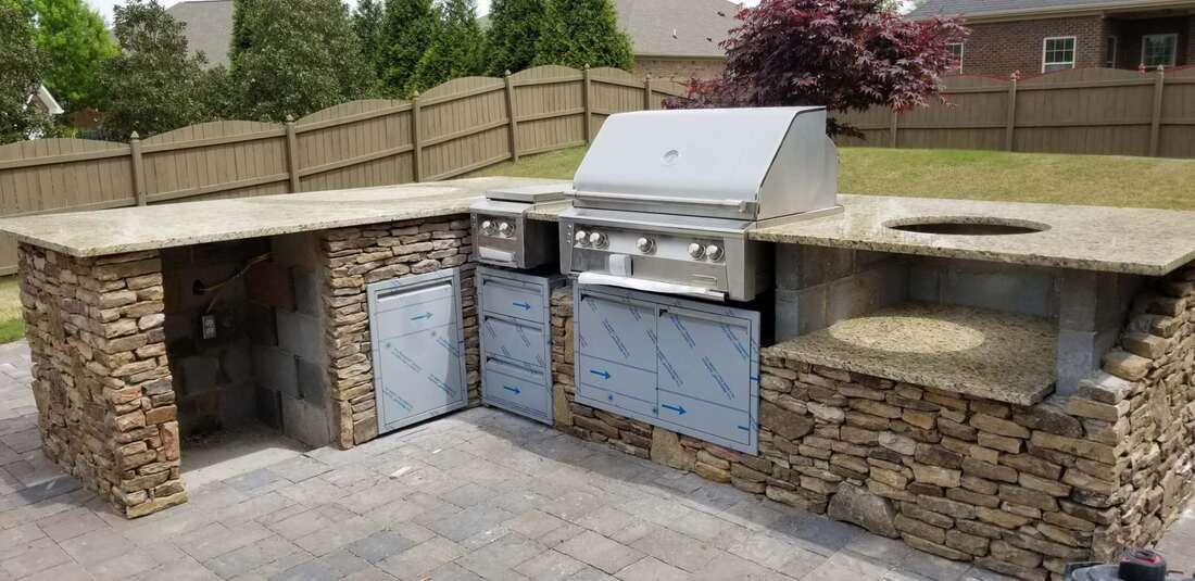 A large outdoor kitchen with a grill and granite counter tops.