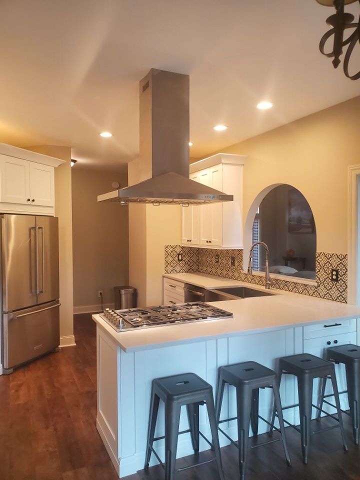 A kitchen with white cabinets , stainless steel appliances , and a large island with stools.