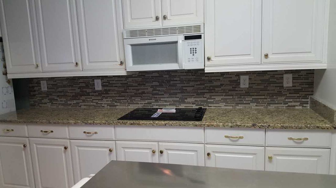 A kitchen with white cabinets , granite counter tops , a microwave , and a stove top oven.