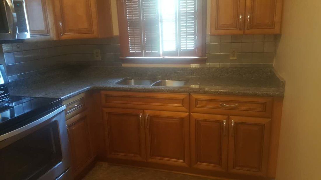 A kitchen with wooden cabinets , granite counter tops , stainless steel appliances and a window.