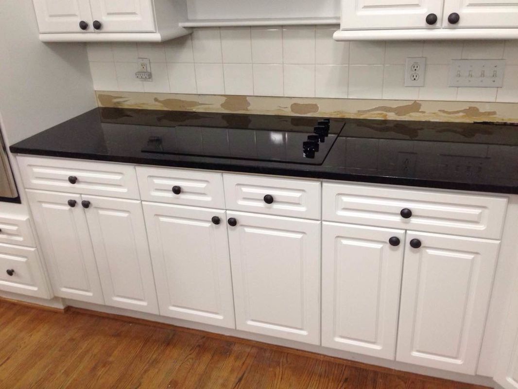 A kitchen with white cabinets and black counter tops.