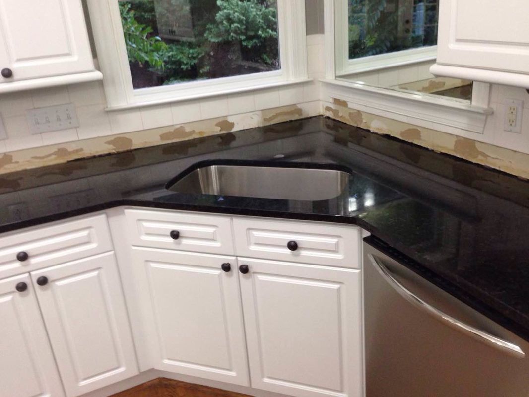 A kitchen with black granite counter tops , white cabinets , and a stainless steel sink.