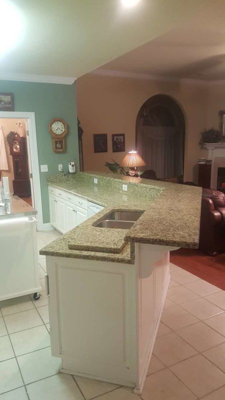 A kitchen with granite counter tops and a sink in a living room.