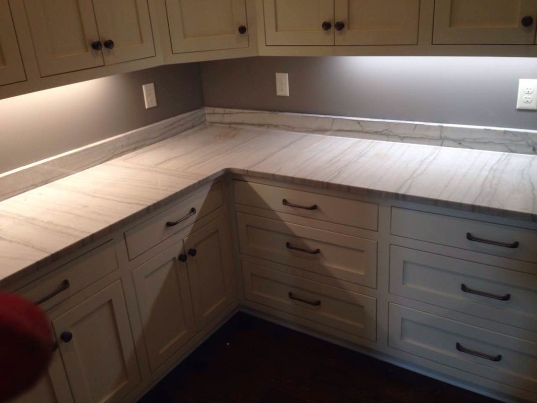 A kitchen with white cabinets and marble counter tops