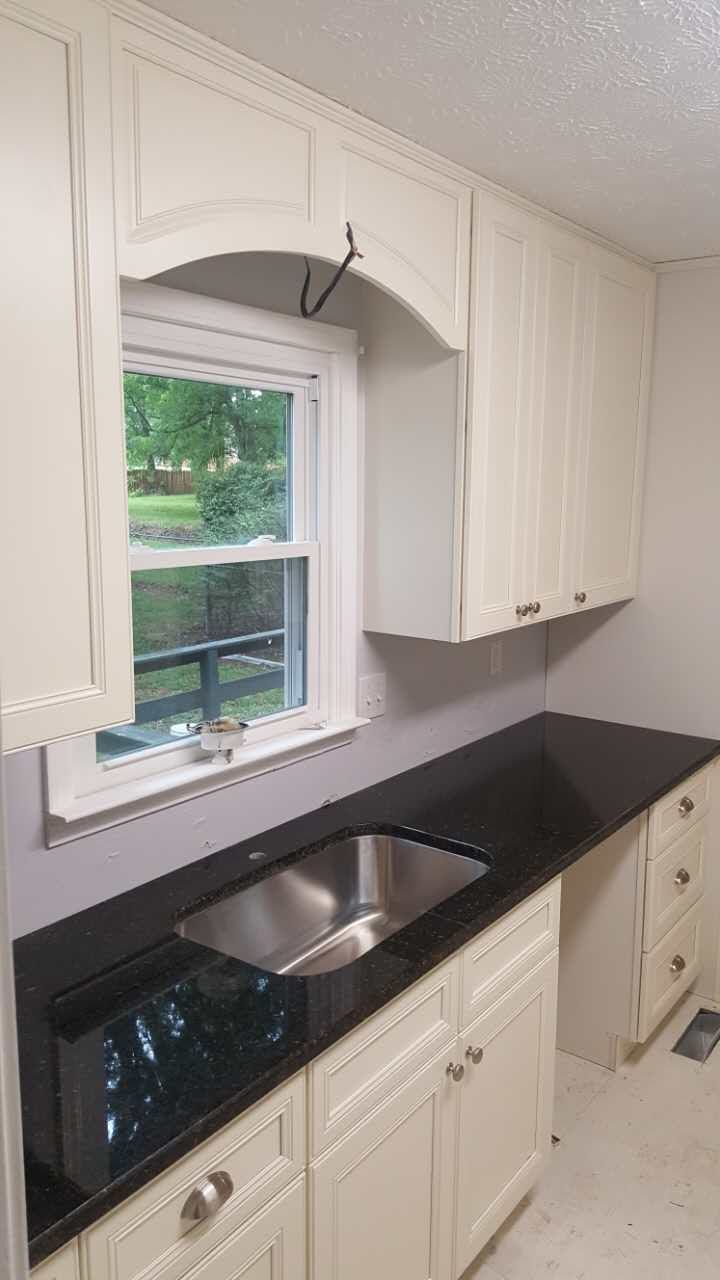 A kitchen with white cabinets , black counter tops , a sink and a window.