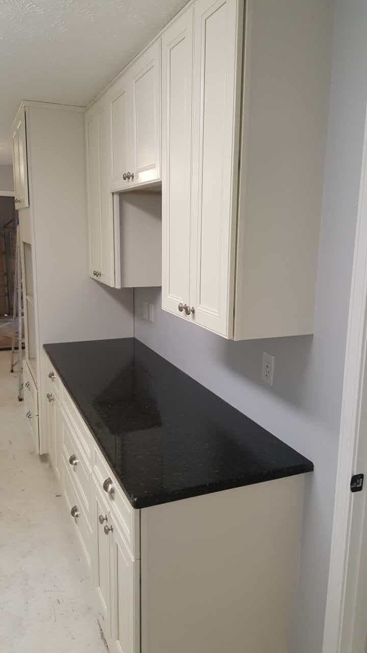 A kitchen with white cabinets and a black counter top.