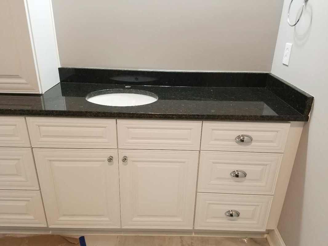 A bathroom vanity with black granite counter tops and white cabinets.