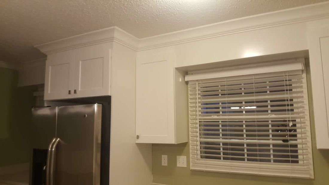 A kitchen with a refrigerator , cabinets , and a window with blinds.