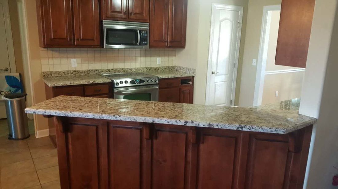 A kitchen with wooden cabinets , granite counter tops , a stove and microwave.