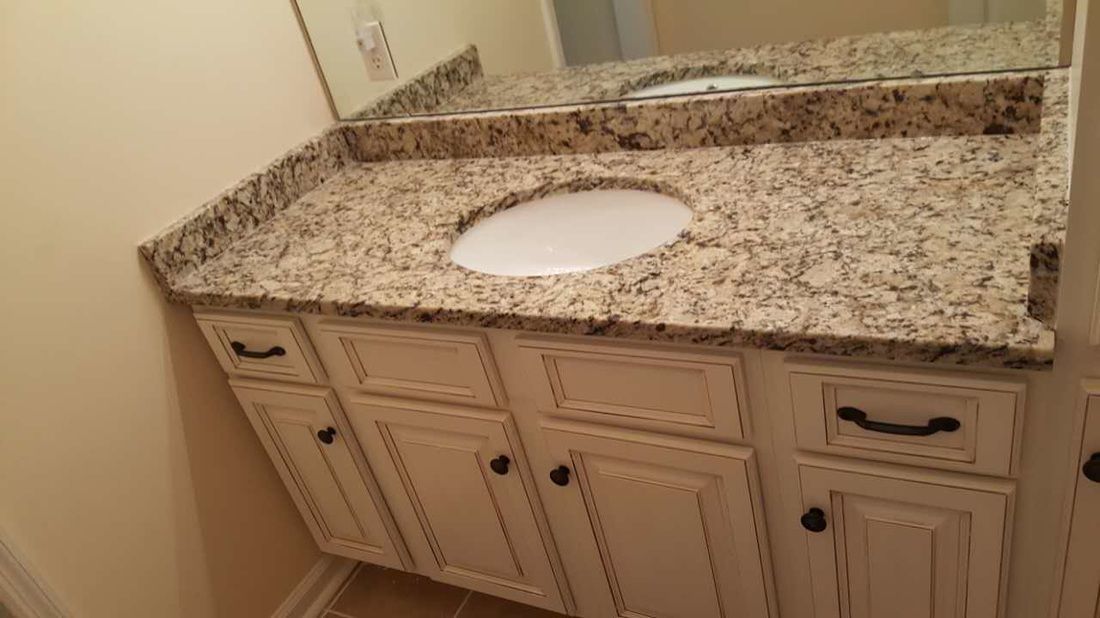A bathroom vanity with a granite counter top and a sink.