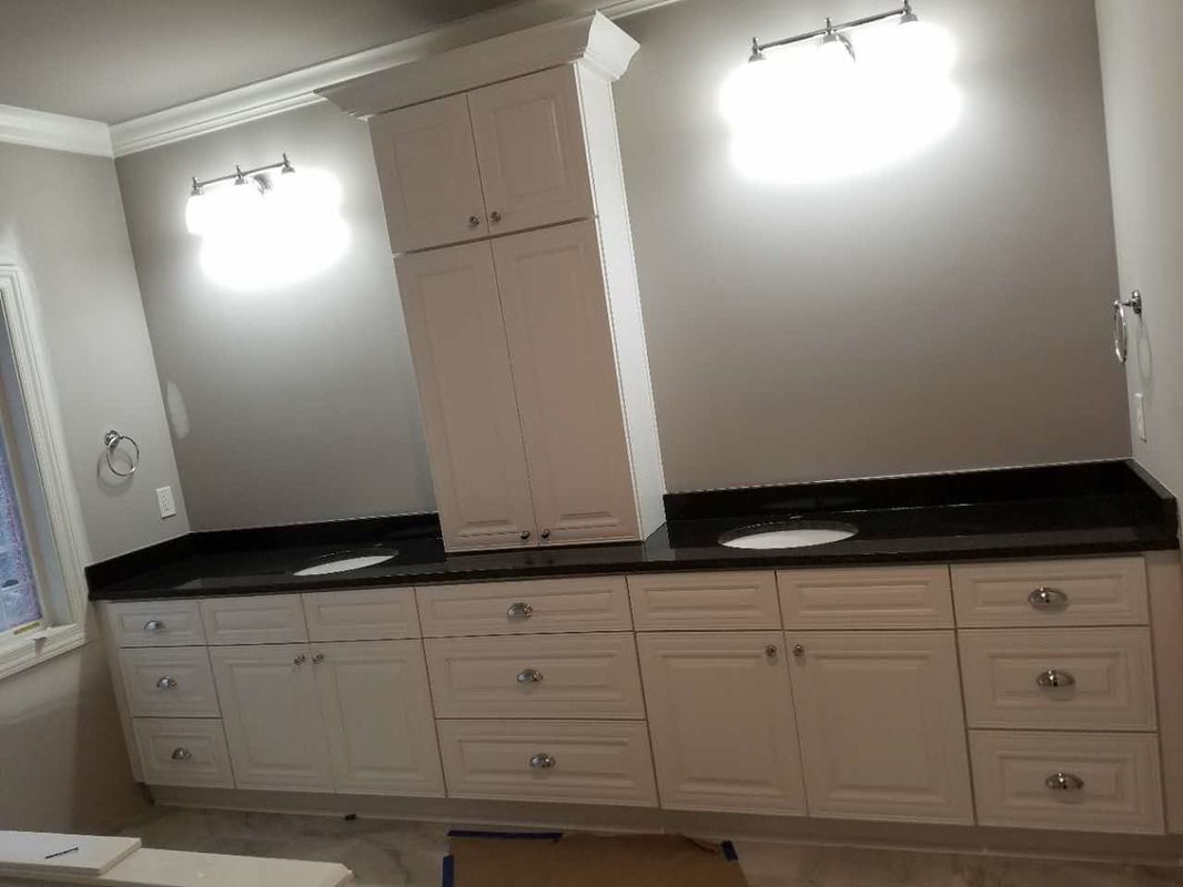 A bathroom with white cabinets and black counter tops