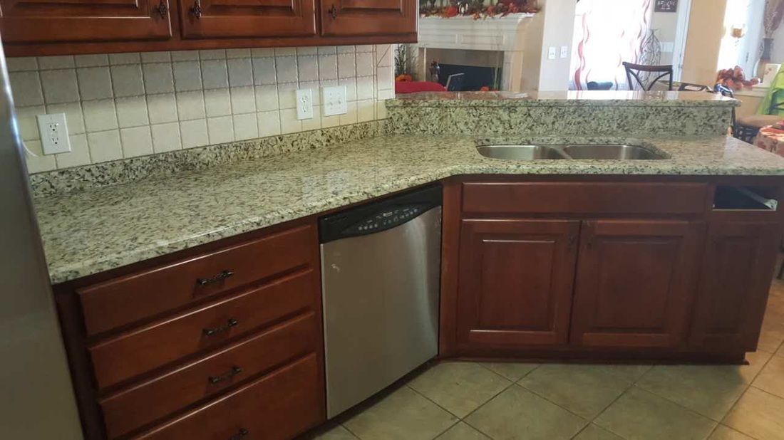 A kitchen with granite counter tops , wooden cabinets , a stainless steel dishwasher and a sink.