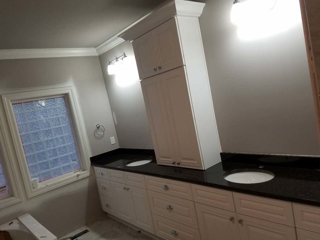 A bathroom with a toilet , sink , cabinets and a window.