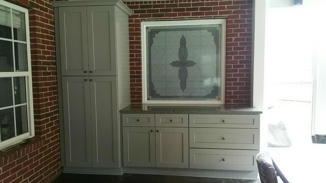 A room with a brick wall , cabinets , drawers and a picture on the wall.