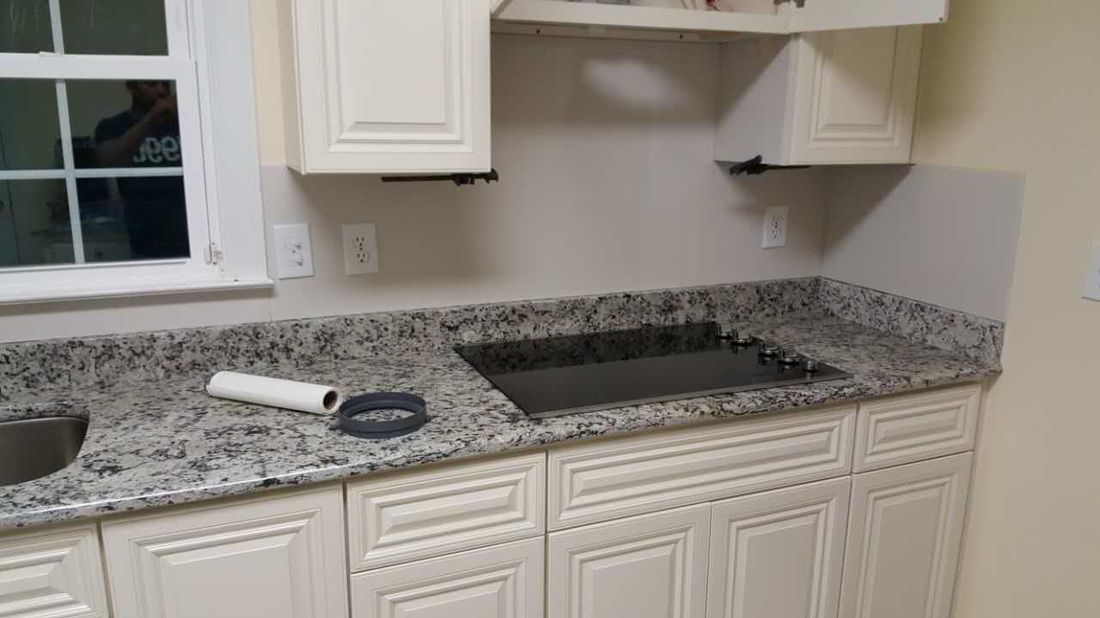 A kitchen with granite counter tops , white cabinets , and a stove top oven.