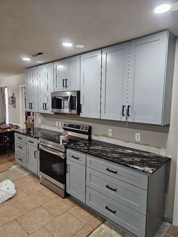 A kitchen with gray cabinets , black counter tops , a stove , and a microwave.