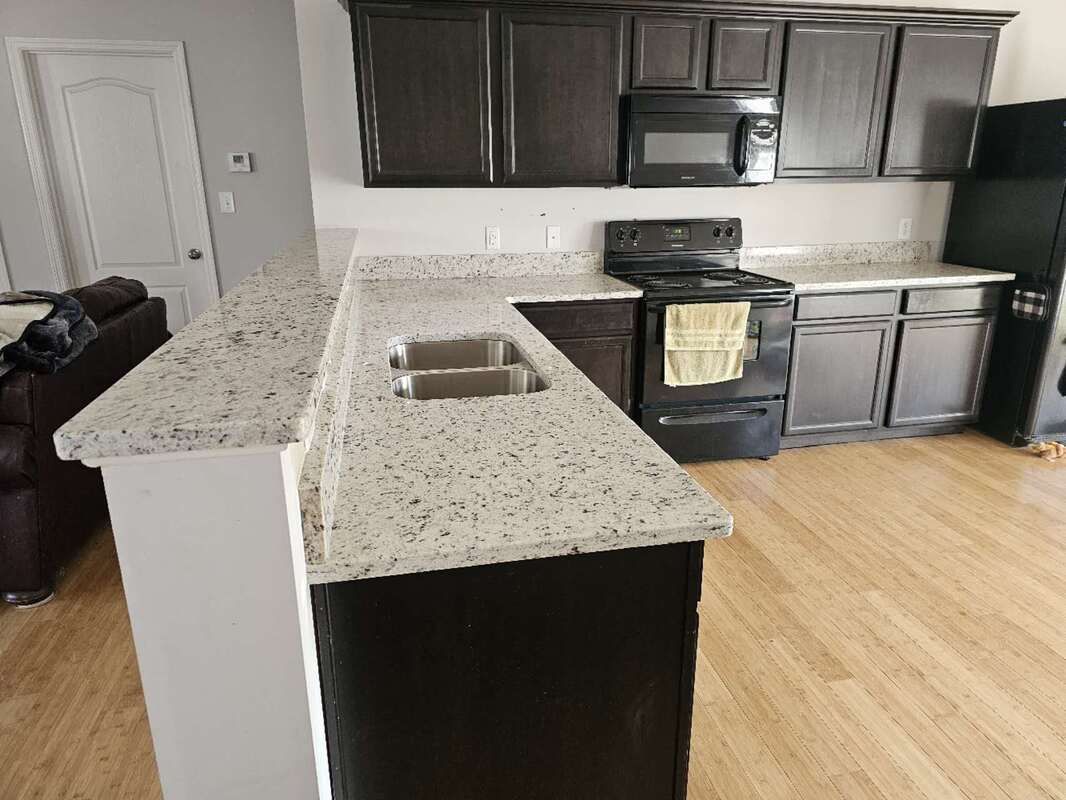 A kitchen with granite counter tops , stainless steel appliances , and black cabinets.
