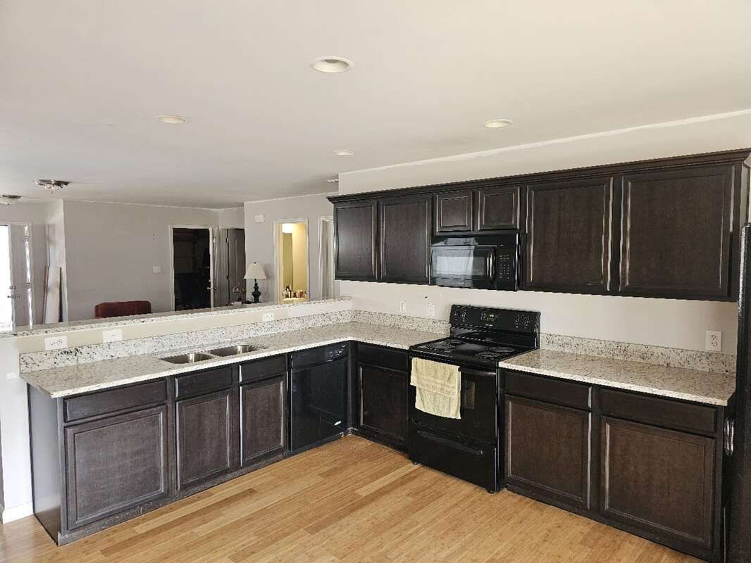 A kitchen with dark cabinets , granite counter tops , a stove and a refrigerator.