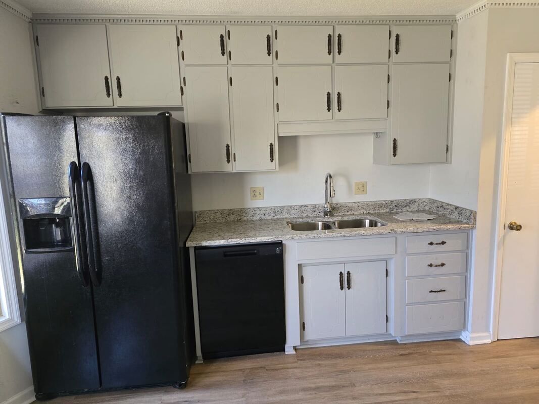 A kitchen with white cabinets and a black refrigerator