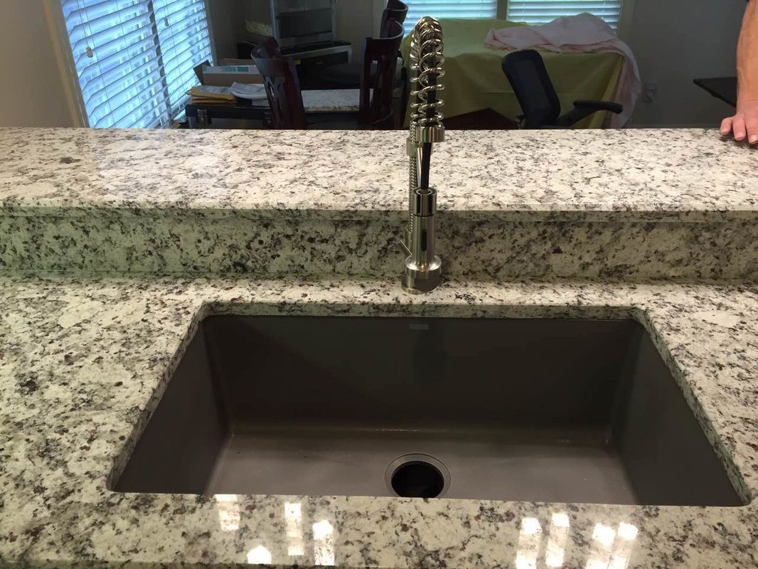 A kitchen sink with a faucet on a granite counter top.