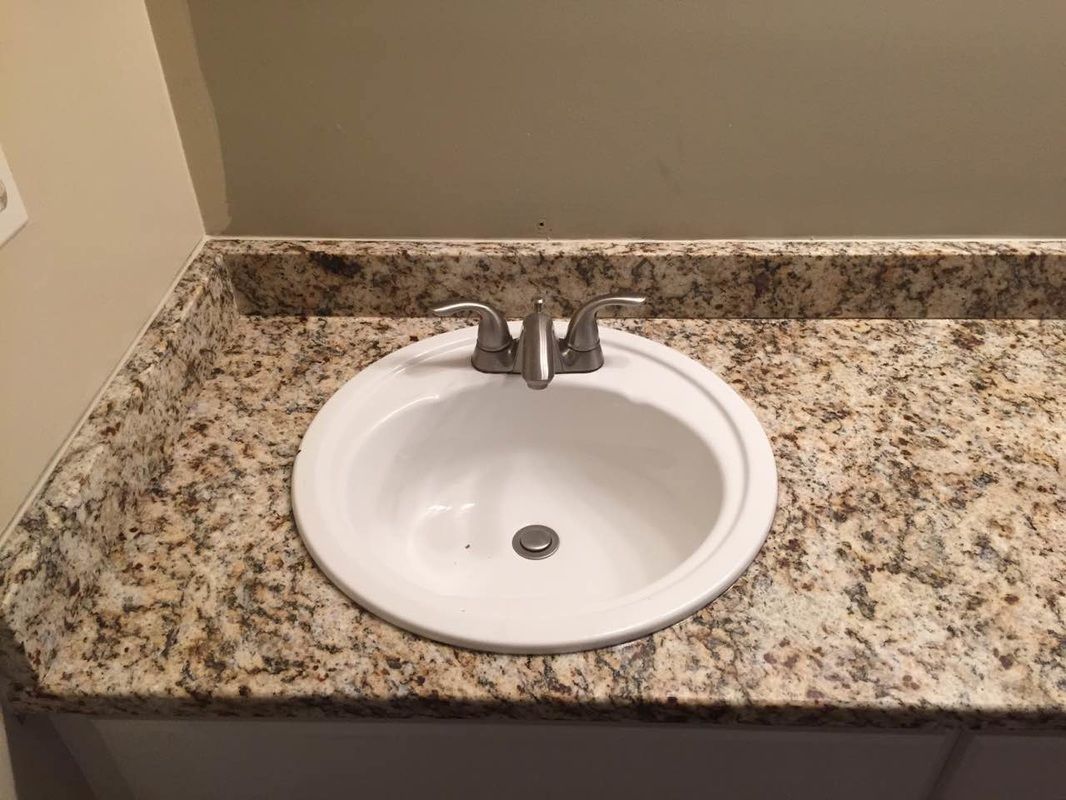 A bathroom sink with a granite counter top and a faucet.