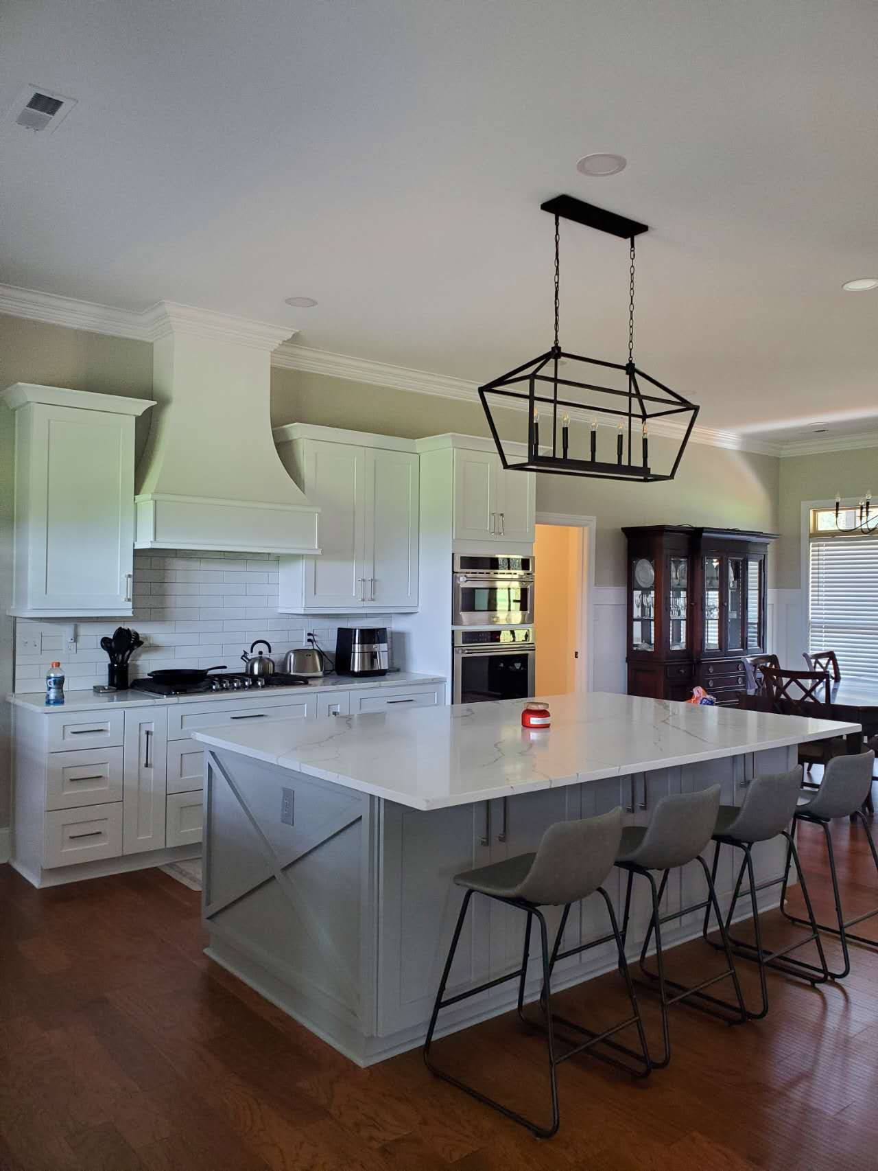 A kitchen with a large island and stools and a chandelier hanging from the ceiling.