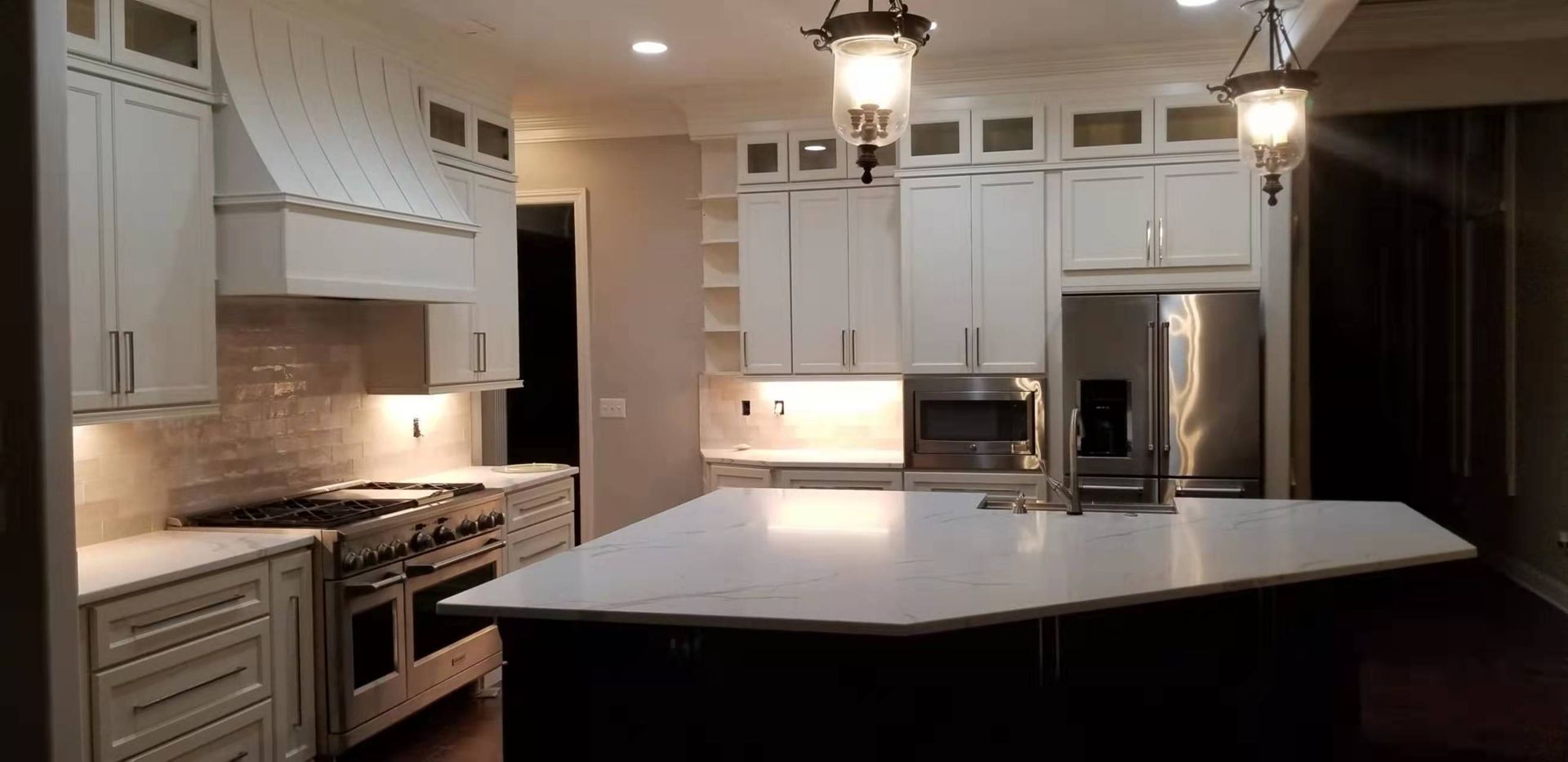 A kitchen with white cabinets , stainless steel appliances , and a large island.
