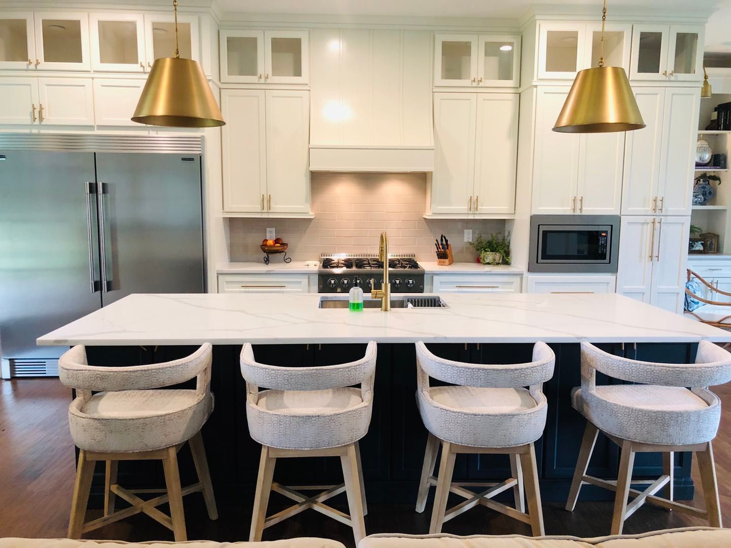 A kitchen with a large island , stools and a refrigerator.