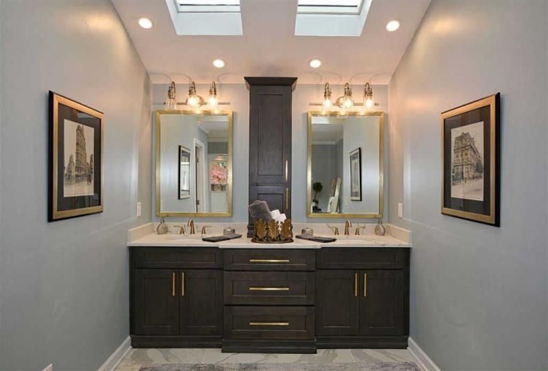 A bathroom with two sinks , two mirrors and a skylight.