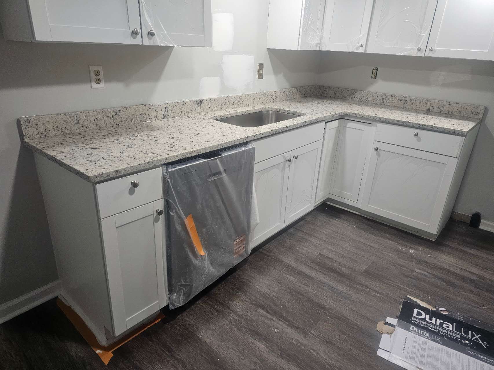 A kitchen with white cabinets, granite counter tops, a sink, and a dishwasher.