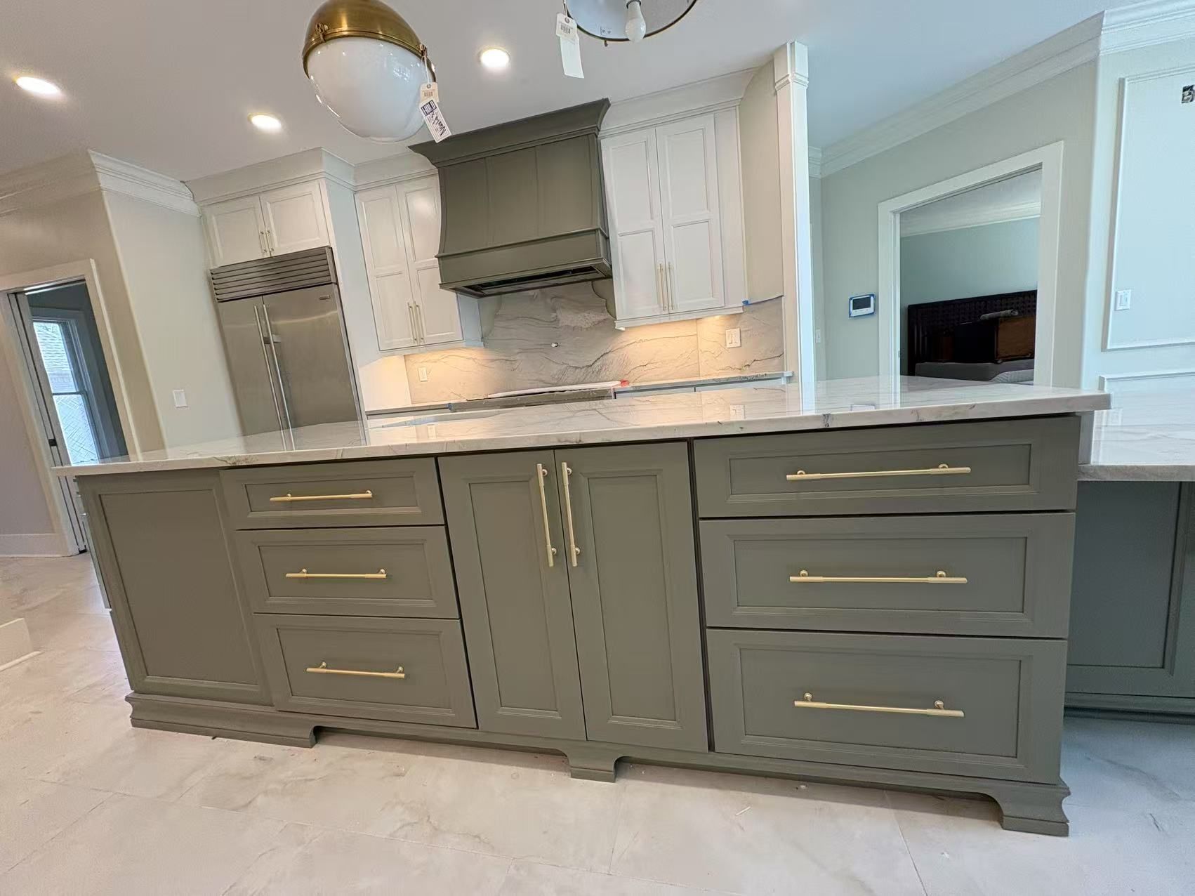 A kitchen with gray cabinets and gold handles and a large island.