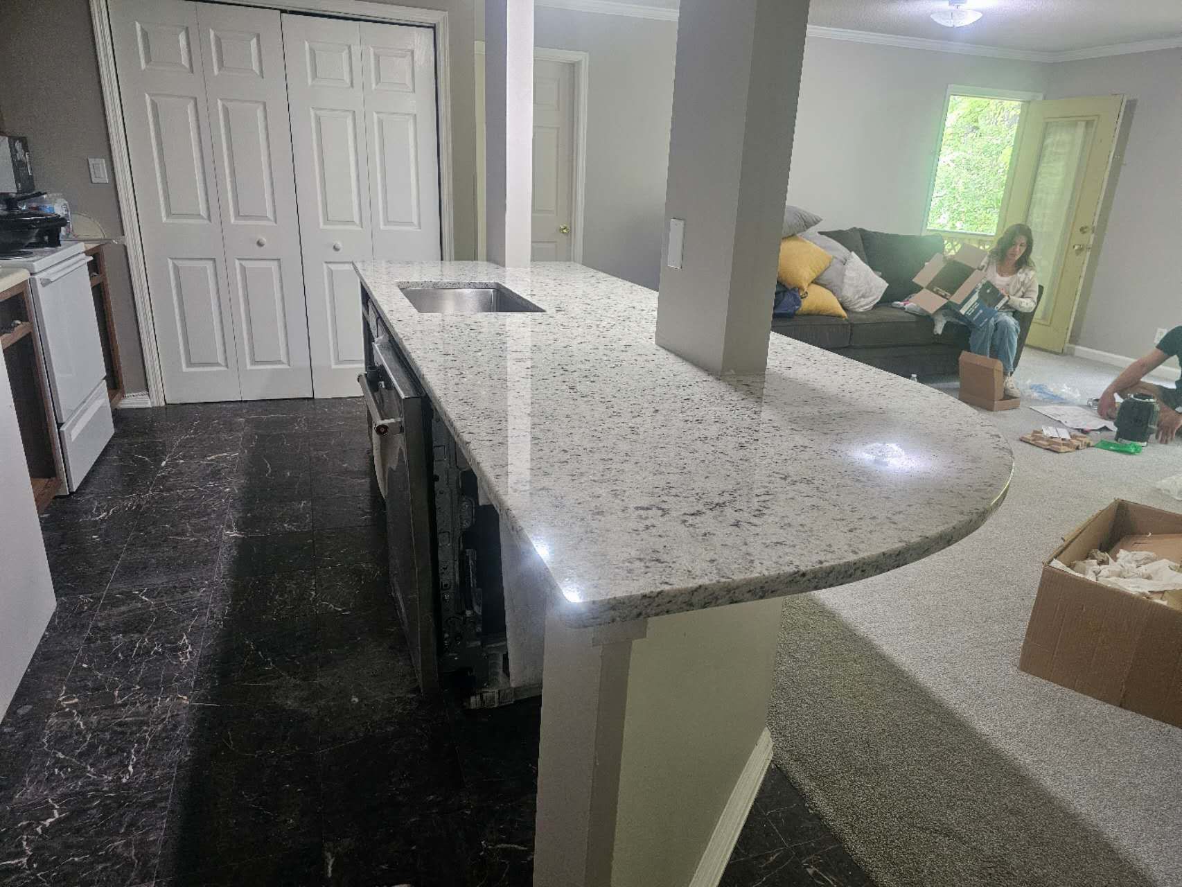 A kitchen with a granite counter top and a couch in the background.