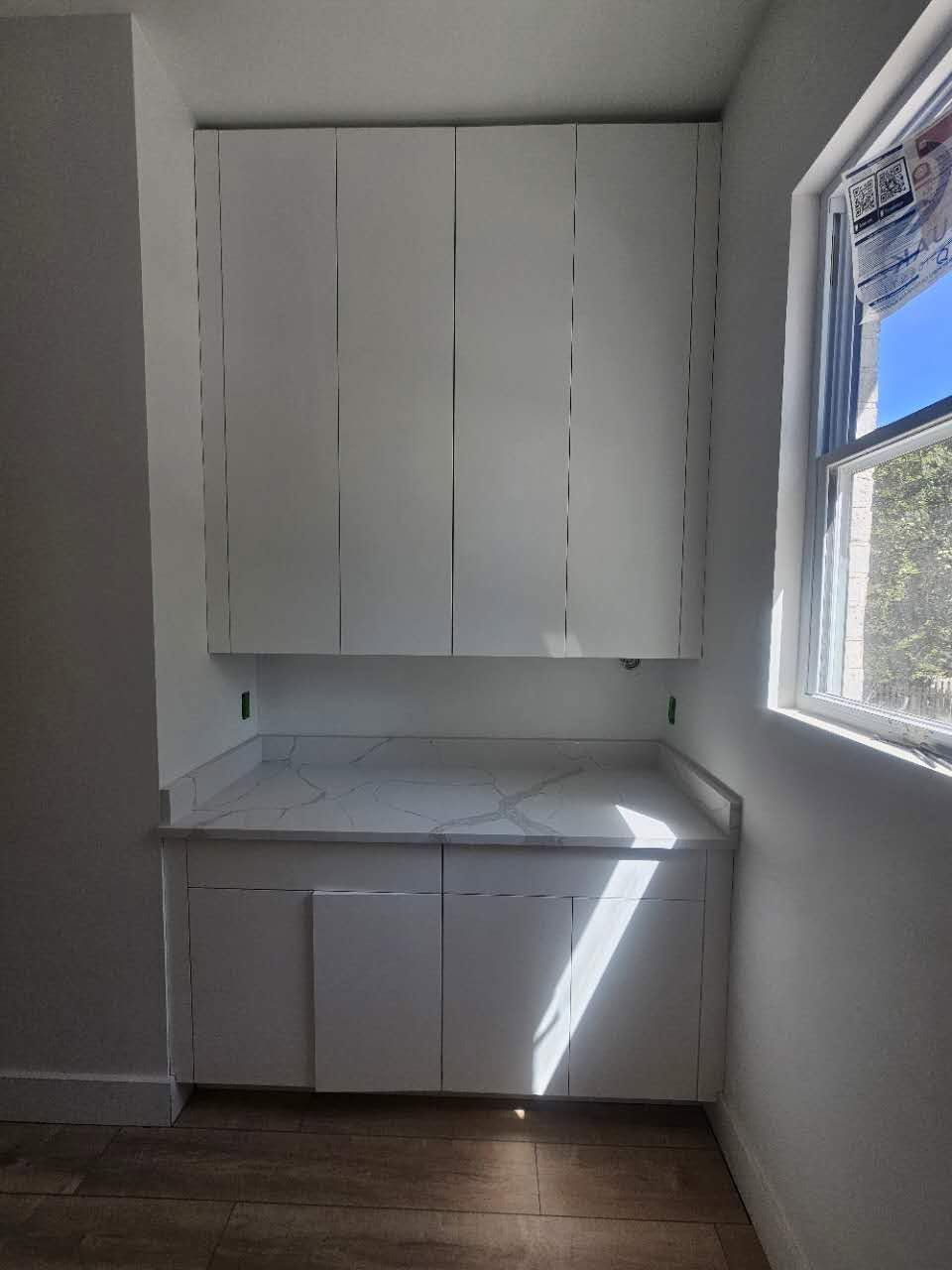 An empty kitchen with white cabinets and a window.